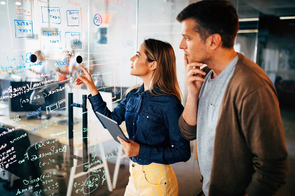 woman and man with a tablet looking at data written on a glass to form a technology strategy