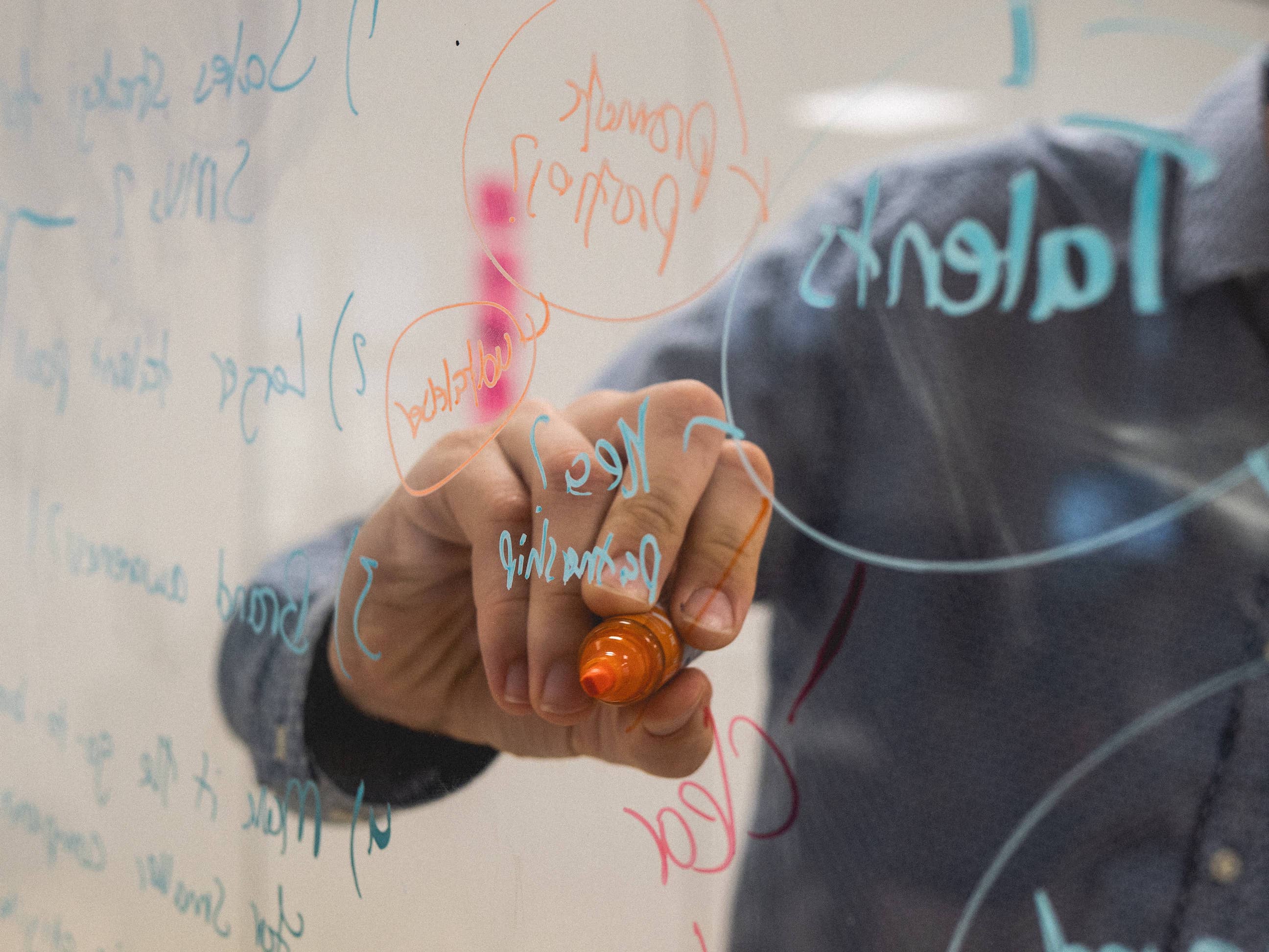 A hand holding an orange marker writes on a clear surface during a workshop.