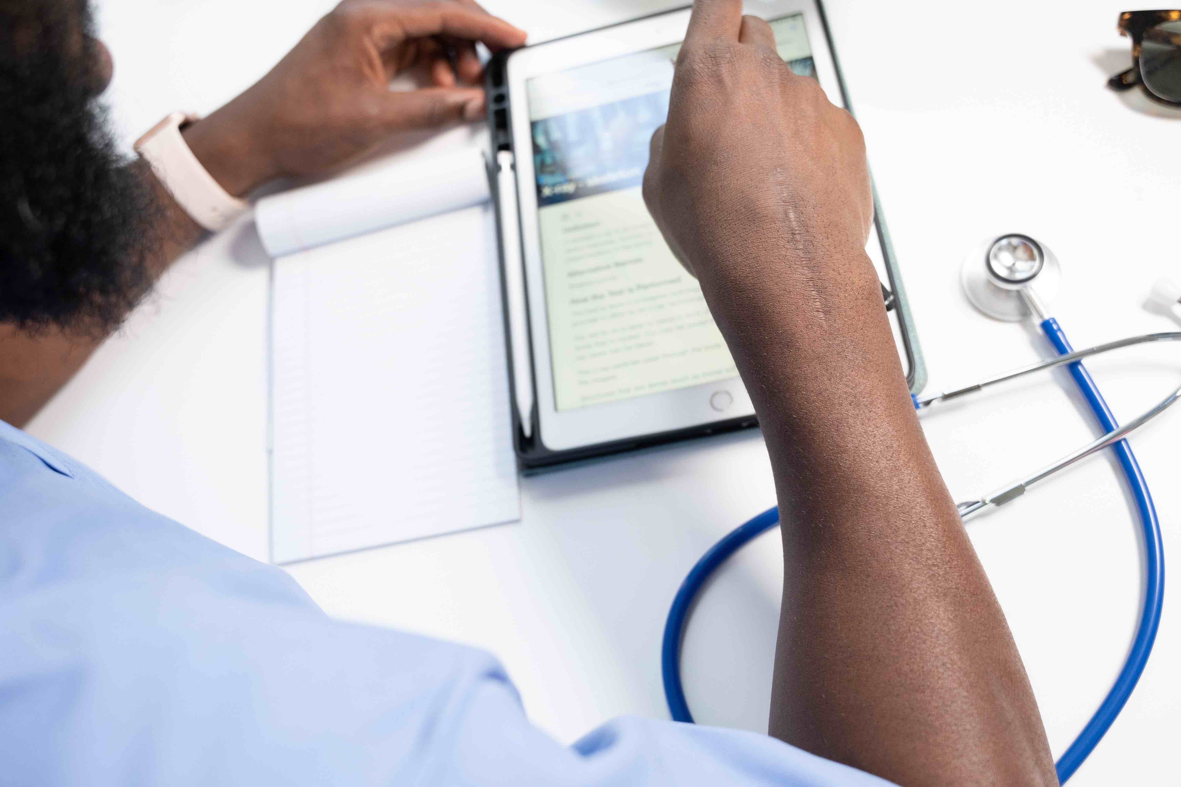 The hands of a medical professional touch a tablet.