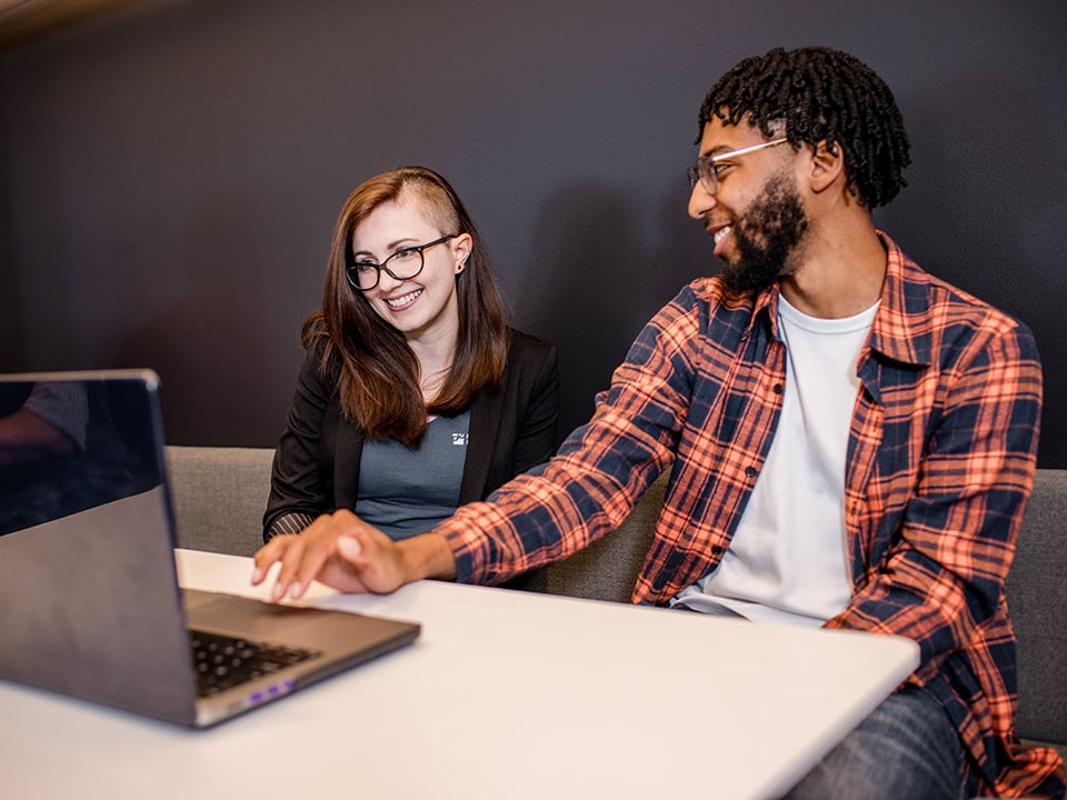 Two P/E team members, talking and looking at a laptop.