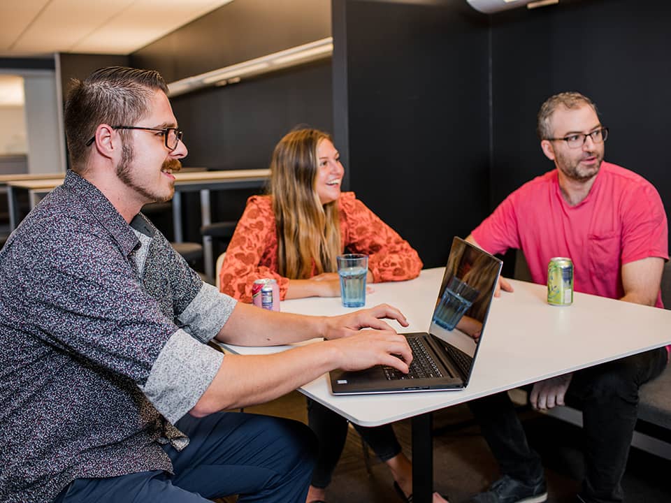 Three people seated at a table at the P/E office.