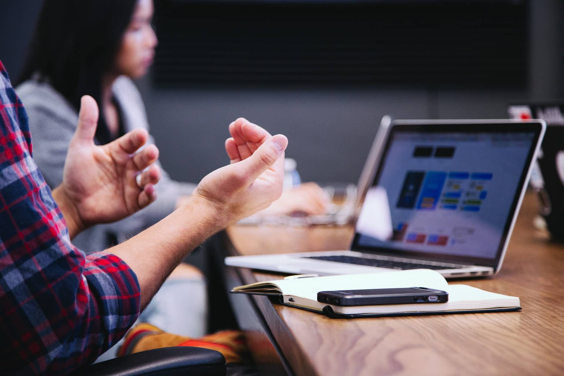 A person in a meeting gestures in front of a laptop and notebook.