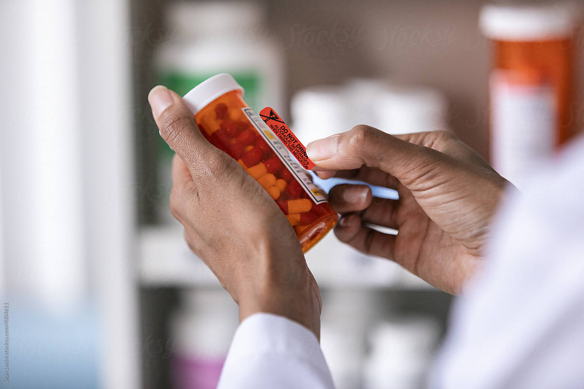 A pharmacist's hands add a label to a prescription medication bottle.