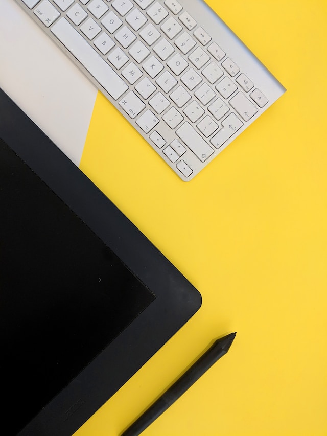 A black tablet and silver keyboard sit on a yellow background.
