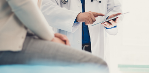 A medical professional uses a tablet while a patient sits in the foreground.