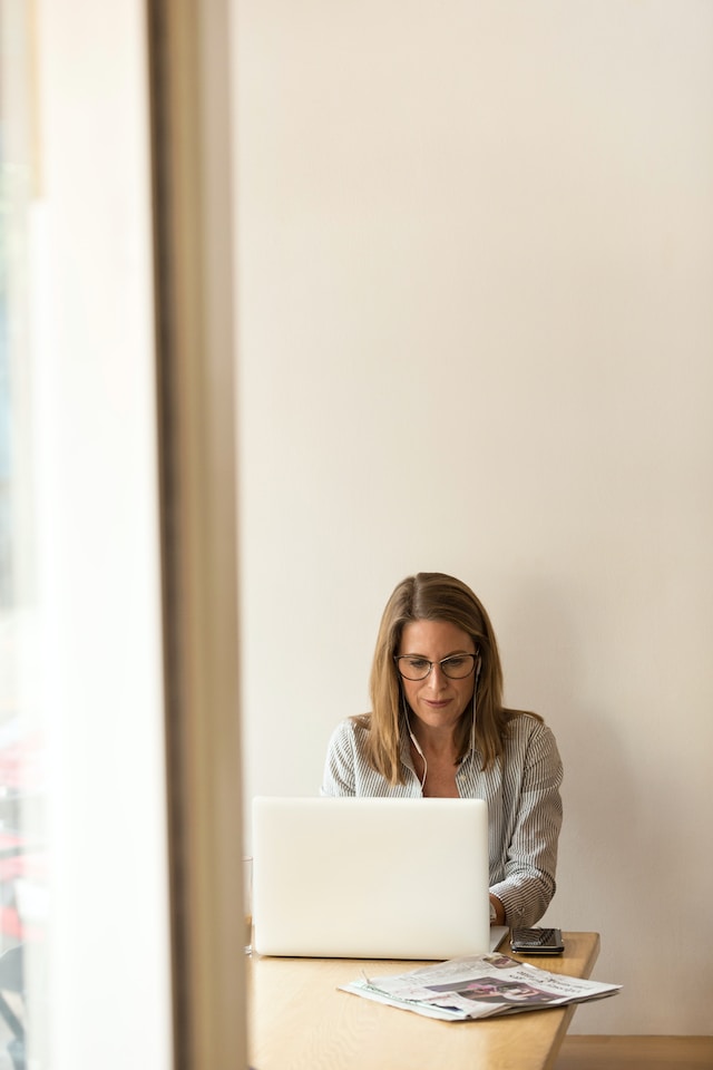 Stock candid image of a woman typing on a laptop while wearing headphones.