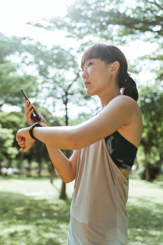 A person dressed in workout clothes looks at their phone and smartwatch.